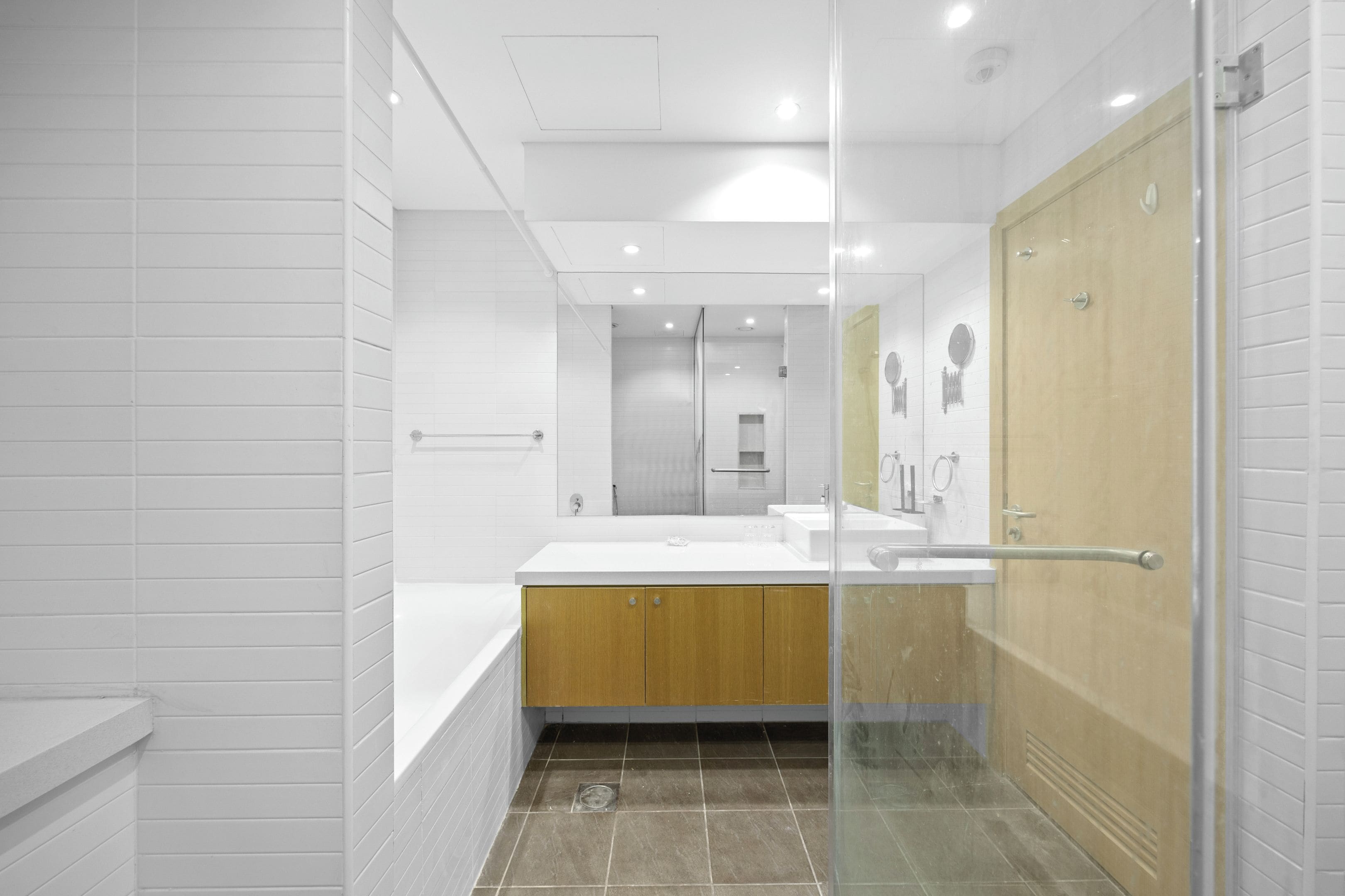 A modern bathroom with a glass shower enclosure, a wooden vanity, and a large mirror.