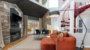 A modern living room with a stone fireplace, a large sectional sofa, and a staircase with red railings. - Mars Hill Retreat: Sauna, Wet Bar, Hot Tub, Views (Mars Hill)