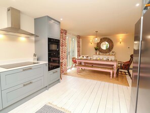 A modern kitchen with grey cabinets, a built-in oven, and a dining area with a wooden table and chairs. - 52 Lee Road (Aldeburgh)
