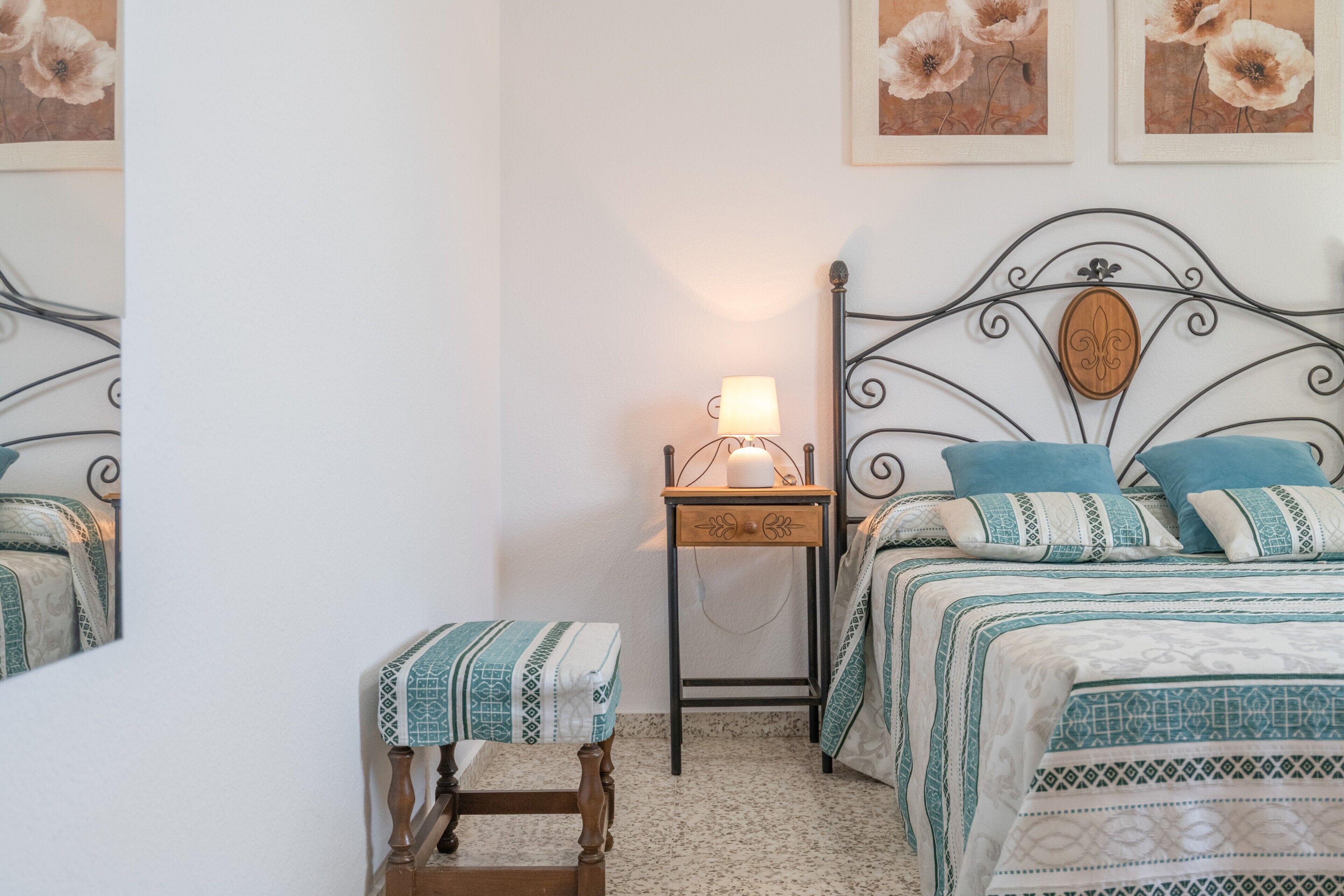 Een slaapkamer met een bed, nachtkastje, lamp en een klein krukje.