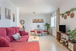 Una sala de estar con un sofá rojo, una mesa de comedor con sillas, un televisor sobre un mueble de madera y obras de arte en las paredes.