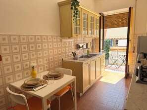 Cucina con zona pranzo, caratterizzata da zoccolo a piastrelle, mobili in legno e un piccolo tavolo con sedie.