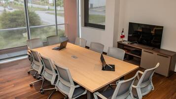 Un salón de conferencias con una mesa grande, seis sillas, un televisor y una ventana que ofrece vistas a una carretera y zonas verdes.