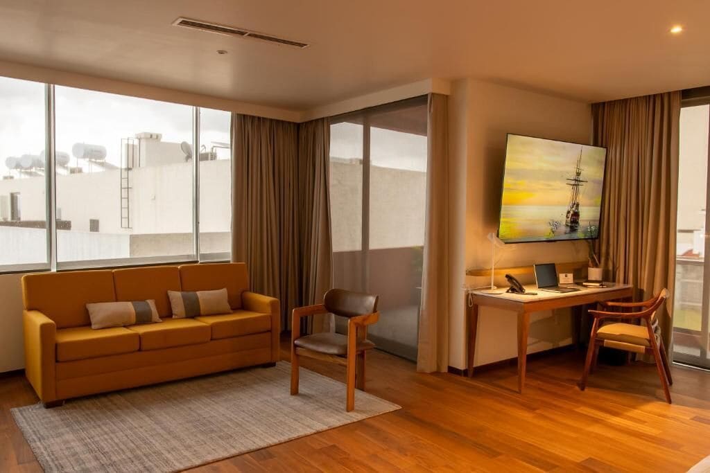 A modern living room with a sofa, chairs, a desk, and a large window with curtains.