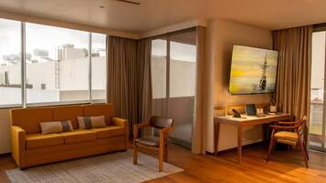 A modern living room with a sofa, chairs, a desk, and a large window with curtains.