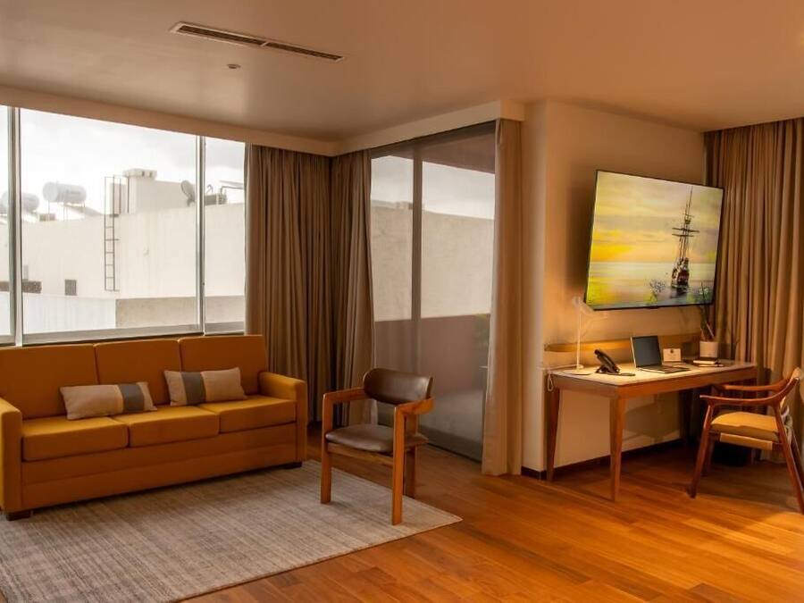 A modern living room with a sofa, chairs, a desk, and a large window with curtains.
