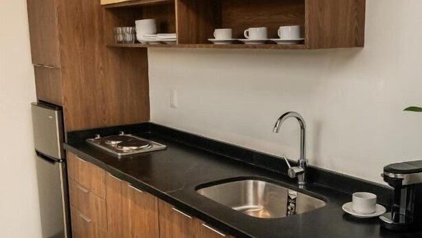 Une cuisine moderne avec des meubles en bois, un plan de travail noir, un évier en acier inoxydable et une machine à café.