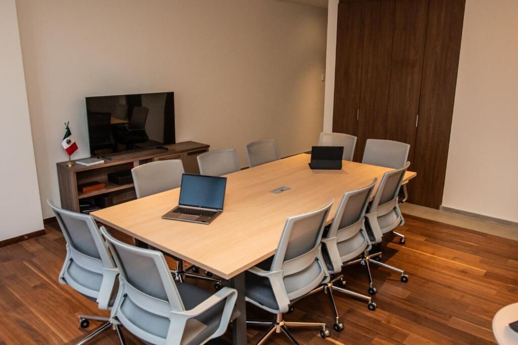 A conference room with a long table, six chairs, a laptop, a television, and a flag.