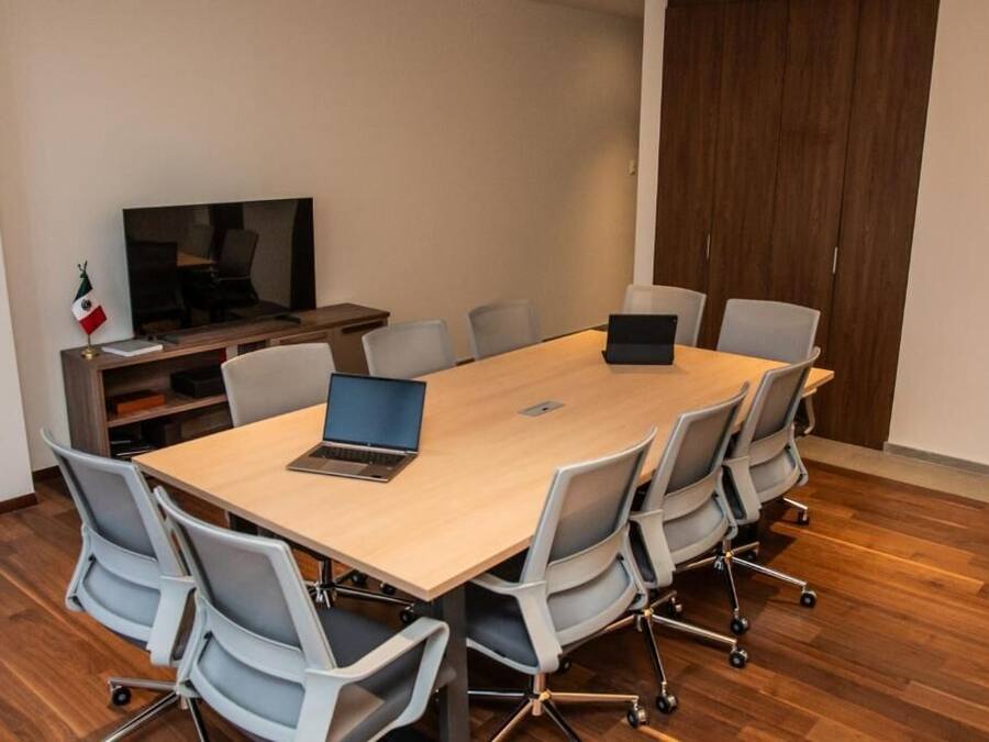 A conference room with a long table, six chairs, a laptop, a television, and a flag.