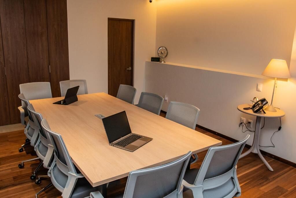 A conference room with a long table, several chairs, a laptop, a clock, and a lamp on a side table.