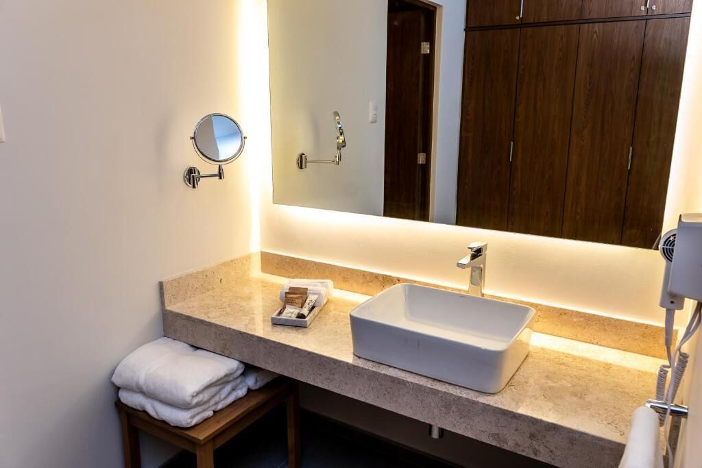 Un baño moderno con un espejo grande, un lavamanos blanco y un perchero para toallas.