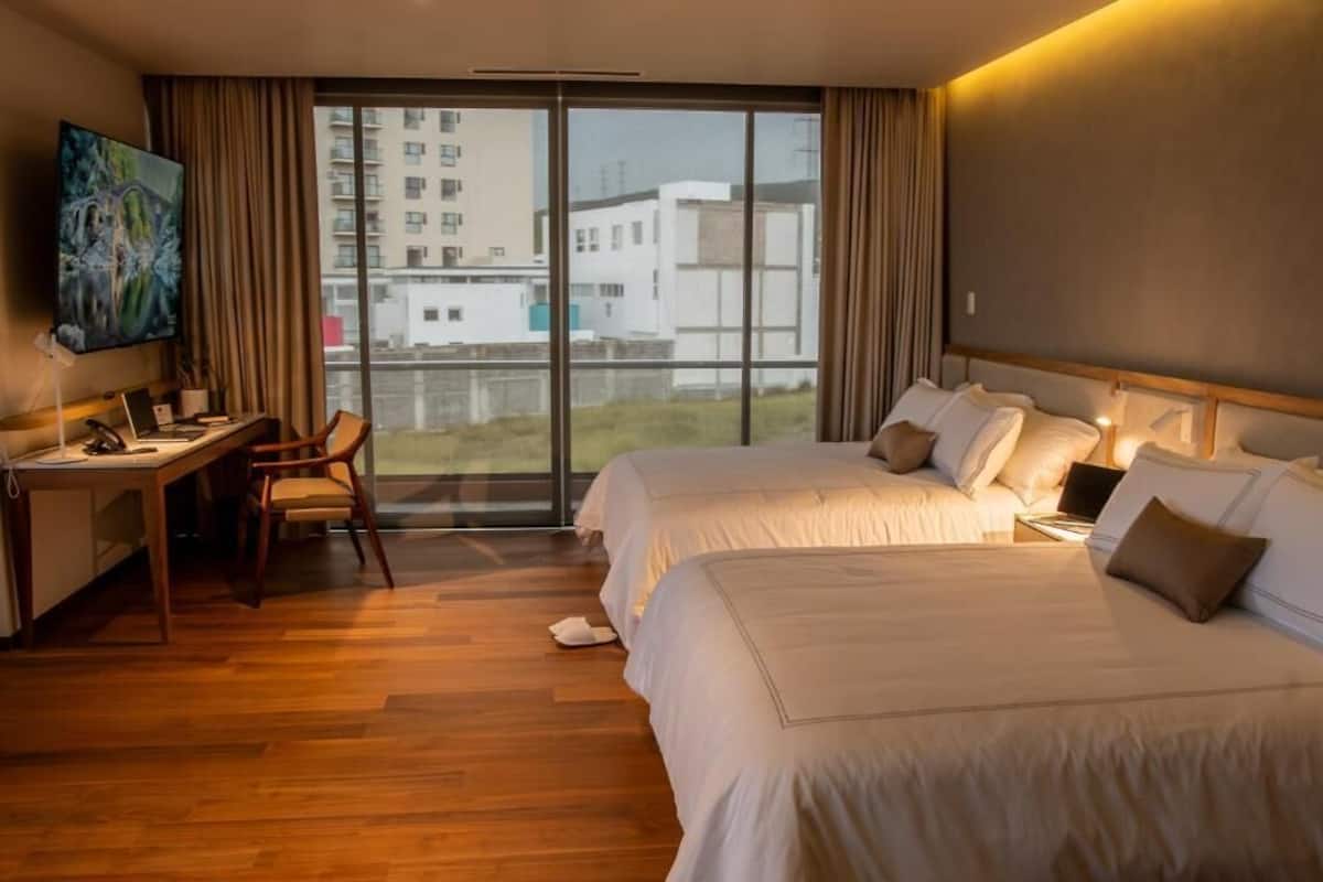 Une chambre d’hôtel avec deux lits, un bureau, une chaise et un téléviseur.