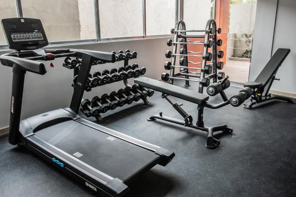 Une salle de sport équipée d’un tapis de course, d’haltères et de poids.