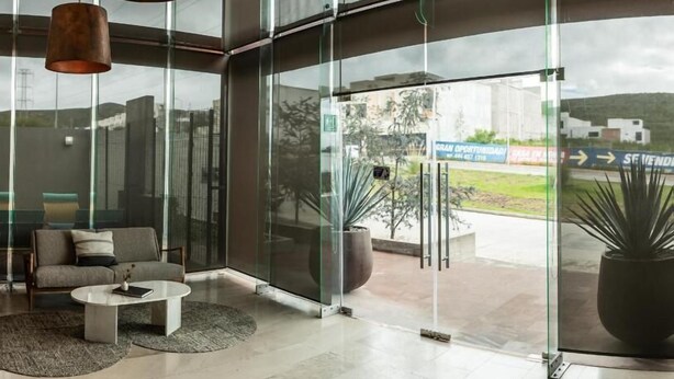Un vestíbulo moderno con un muro de vidrio, un sofá, una mesa de centro y lámparas colgantes.