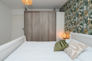 A bedroom with a bed, a wooden wardrobe, a nightstand with a lamp, and a wall with a leaf pattern. - Apartment “Laïta - Stay in Quimperlé” with Private Terrace, Garden, and Wi-Fi (Quimperle)