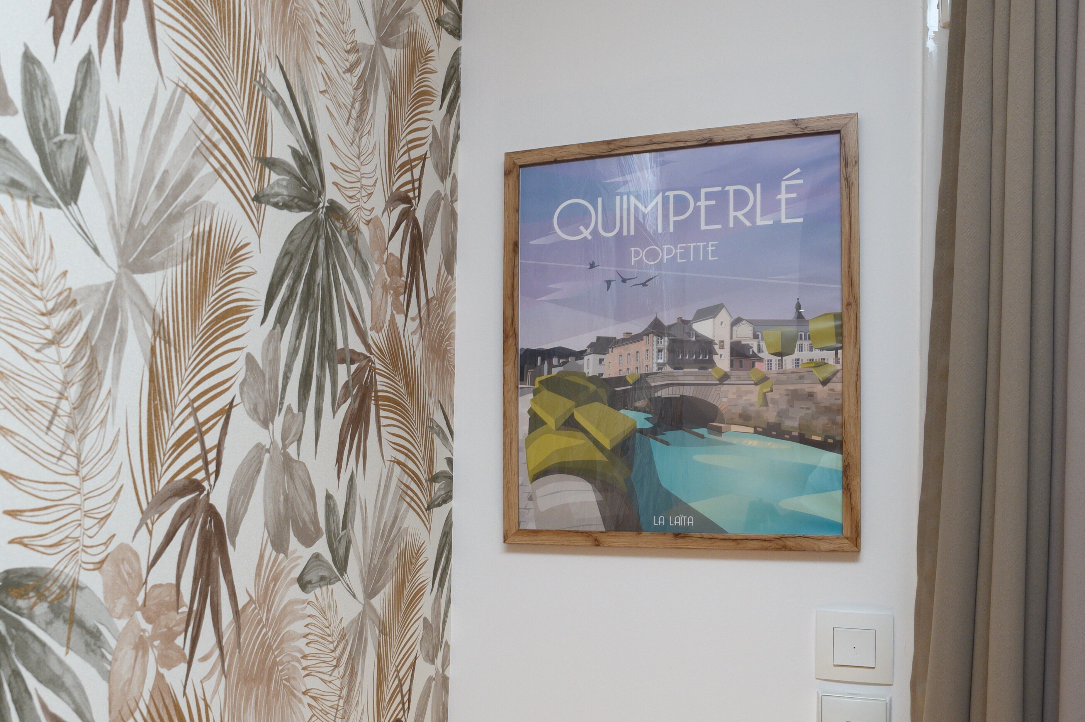 Una obra d'art emmarcada titulada 'QUIMPERLÉ POPETTE' penja d'una paret.