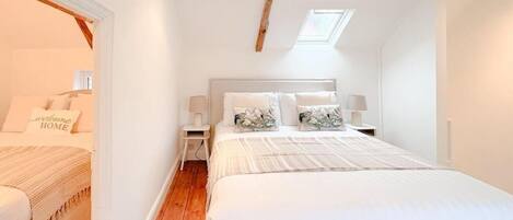 A bedroom with a large bed, a skylight, a wooden floor, and a nightstand with a lamp.