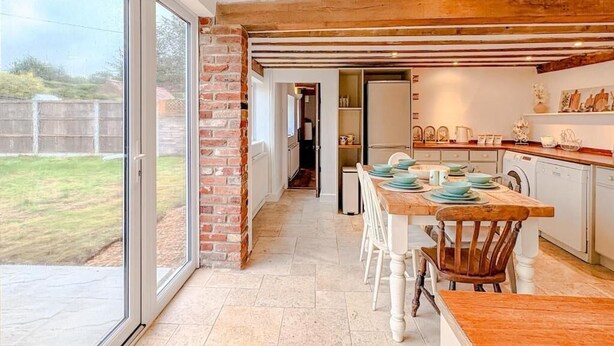 A modern kitchen with a large window, a brick wall, and a wooden ceiling. - Hainford Cottage (Waterloo)