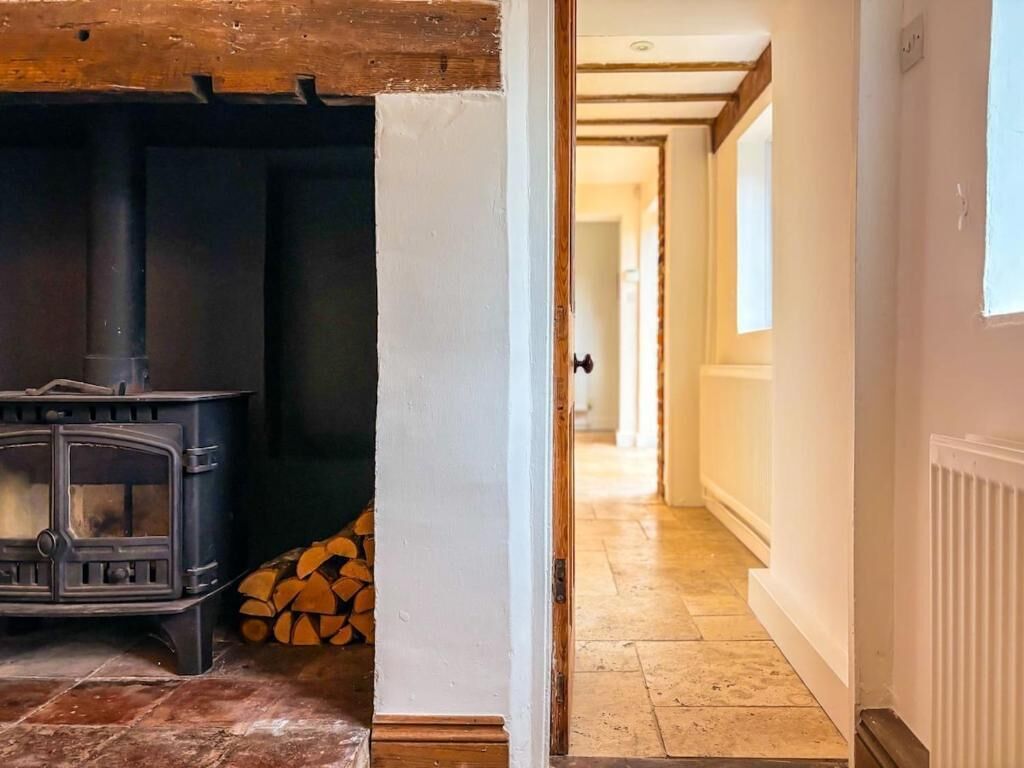 Een kamer met een houtkachel, een deur naar een gang en een radiator aan de muur.