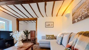 A cozy living room with a wooden ceiling, a grey sofa, a television, and a vase of white flowers. - Hainford Cottage (Waterloo)