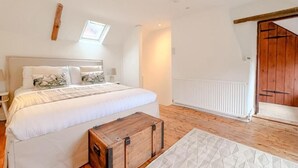 A bedroom with a large bed, a wooden chest, a radiator, and a wooden door. - Hainford Cottage (Waterloo)