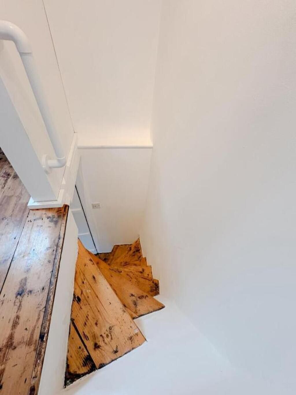 A narrow staircase with wooden steps and white walls.