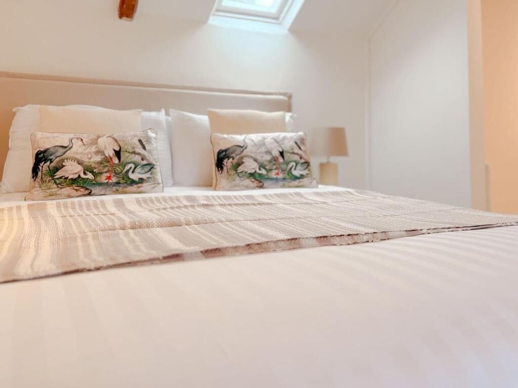 A neatly made bed with floral pillows and a striped blanket, a bedside lamp, and a skylight above.