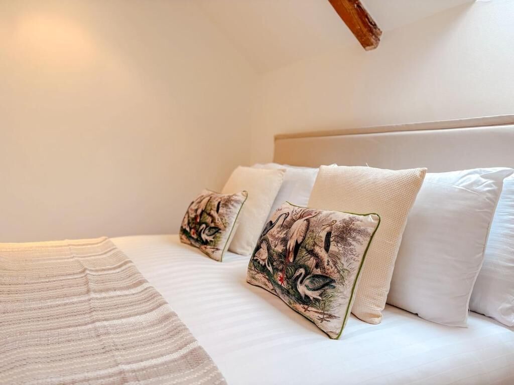 Een net opgemaakt bed met drie kussens, waarvan één met een natuurprint en twee witte kussens.