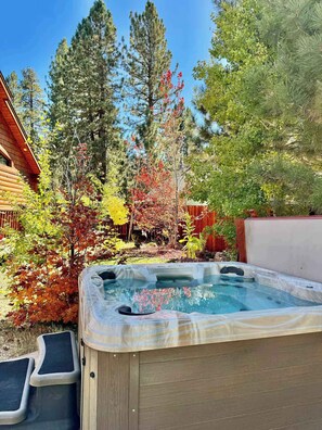Un bain à remous dans un jardin, avec une terrasse en bois, entouré d’arbres et d’un chalet en bois.