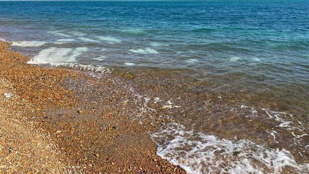 Une plage de galets avec une eau claire et une mer calme.