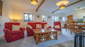 Un salon spacieux avec des canapés rouges à motifs, une table basse en bois et un coin repas comprenant des chaises et une table en bois.