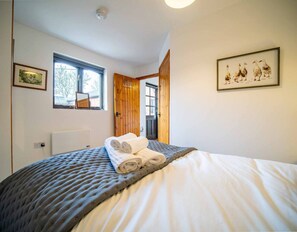 A bedroom with a large bed, a window, a door, and a framed picture on the wall. - Goose Shed | Rural Farm Cottage | Cosy Fire (Stelling Minnis)