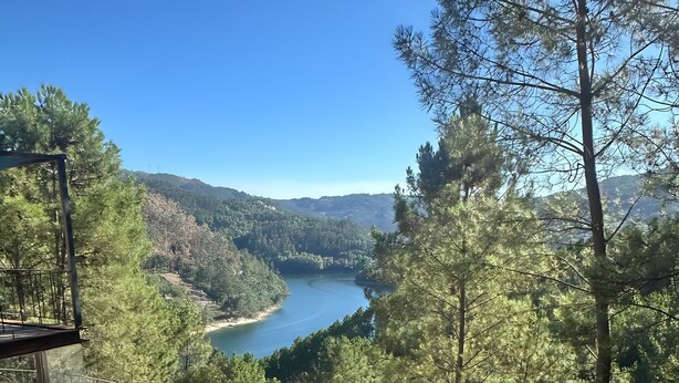 Une terrasse dallée de pierres, avec une rambarde en métal, qui offre une vue sur une rivière et des collines boisées.