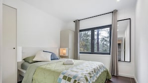 Une chambre à coucher avec un lit, une table de chevet, une fenêtre avec des rideaux et une vue sur les arbres.