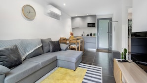 Un salon moderne avec un canapé gris, une table basse en bois et un coin cuisine à l’arrière-plan.