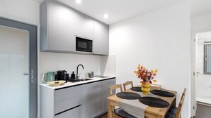 A modern kitchen with a microwave, sink, and dining area with chairs and a table. - Casa do Martinho: Mountain Retreat with Lake View, Shared Terrace, and Wi-Fi (Vilar da Veiga)