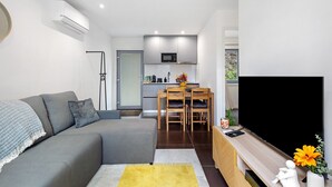 A modern living room with a grey sofa, a wooden dining table, and a flat-screen TV. - Casa do Martinho: Mountain Retreat with Lake View, Shared Terrace, and Wi-Fi (Vilar da Veiga)