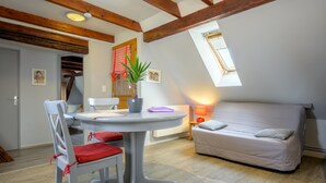 Ein Zimmer mit Esstisch, Stuhl, Sofa, Blumentopf und Fenster.