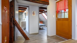 Ein Zimmer mit einer Holztreppe, einer Tür mit Herzdeko und einem Fenster mit rotem Karovorhange.