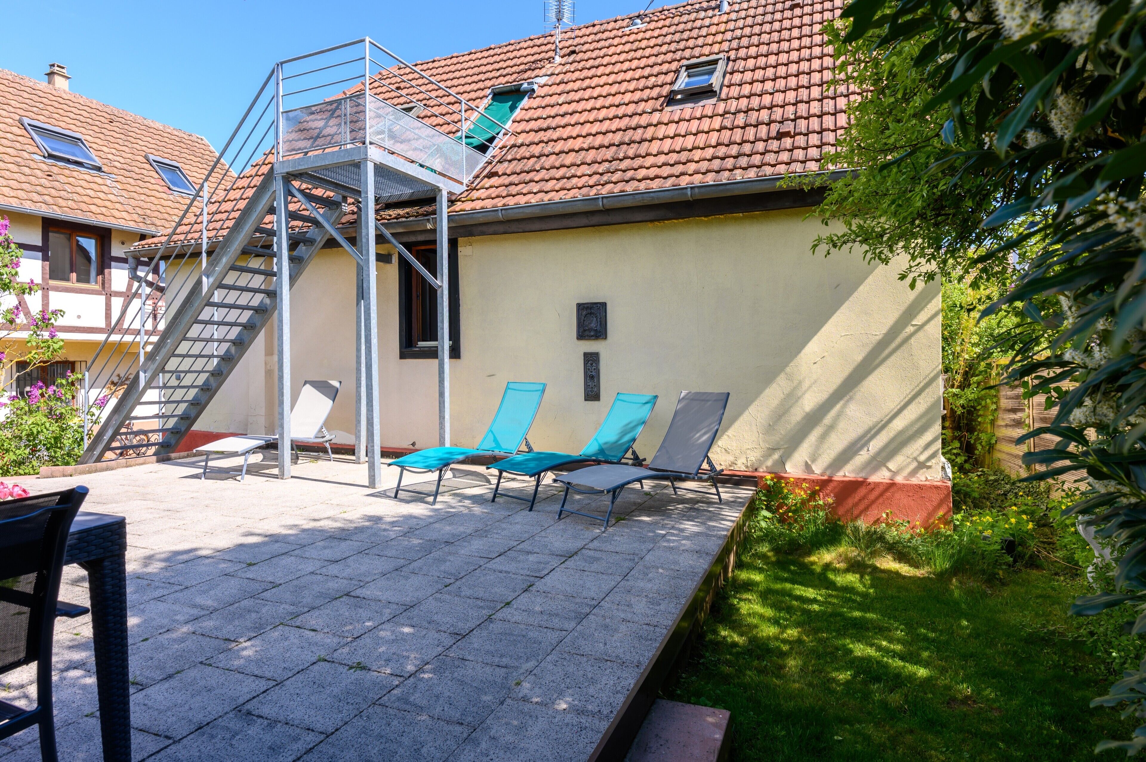 Ein Gebäude mit Ziegeldach, einer Treppe und Sitzgelegenheiten mit Stühlen.