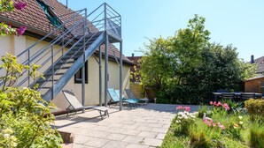 Ein Wohngebäude mit Treppe, Außenbereich zum Sitzen und einem Garten mit verschiedenen Pflanzen und Blumen.