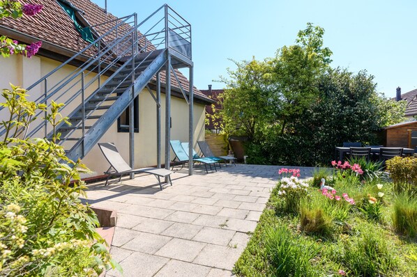 A residential building with a staircase, outdoor seating, and a garden with various plants and flowers.