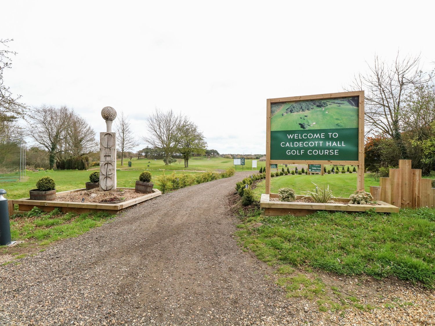 Ein Kiesweg führt zu einem Eingang des Golfplatzes, mit einem Willkommensschild.