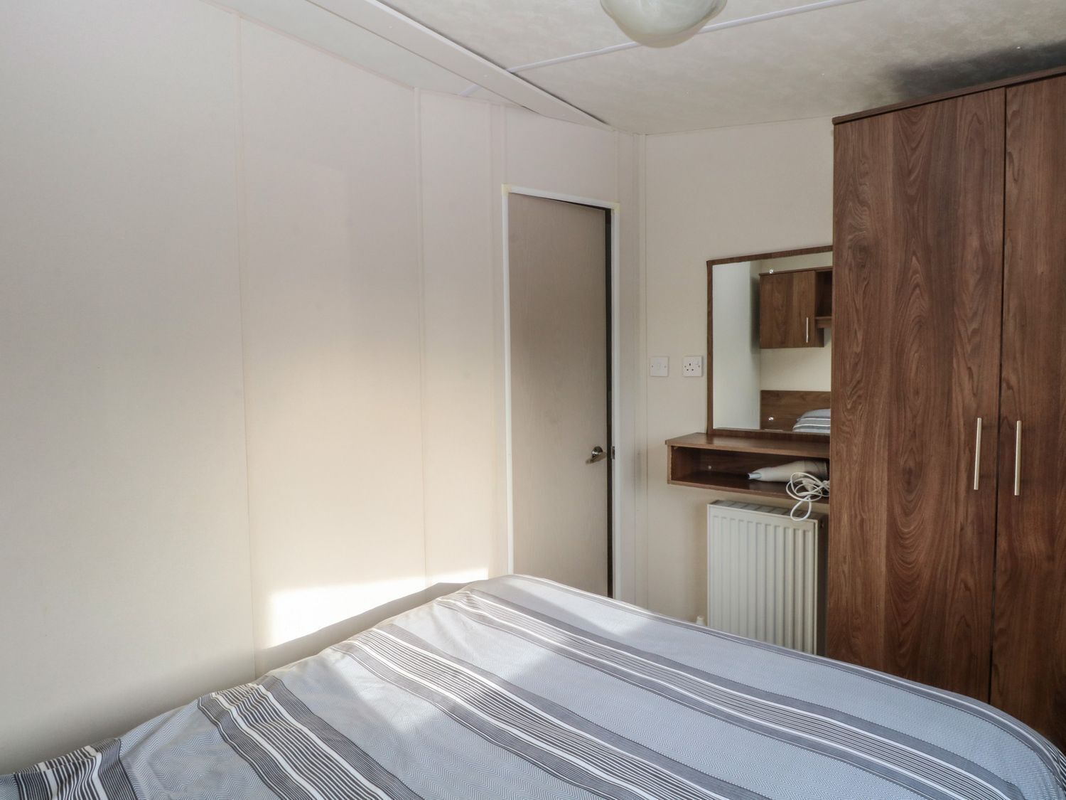 A bedroom with a bed, a wooden wardrobe, a radiator, and a door.