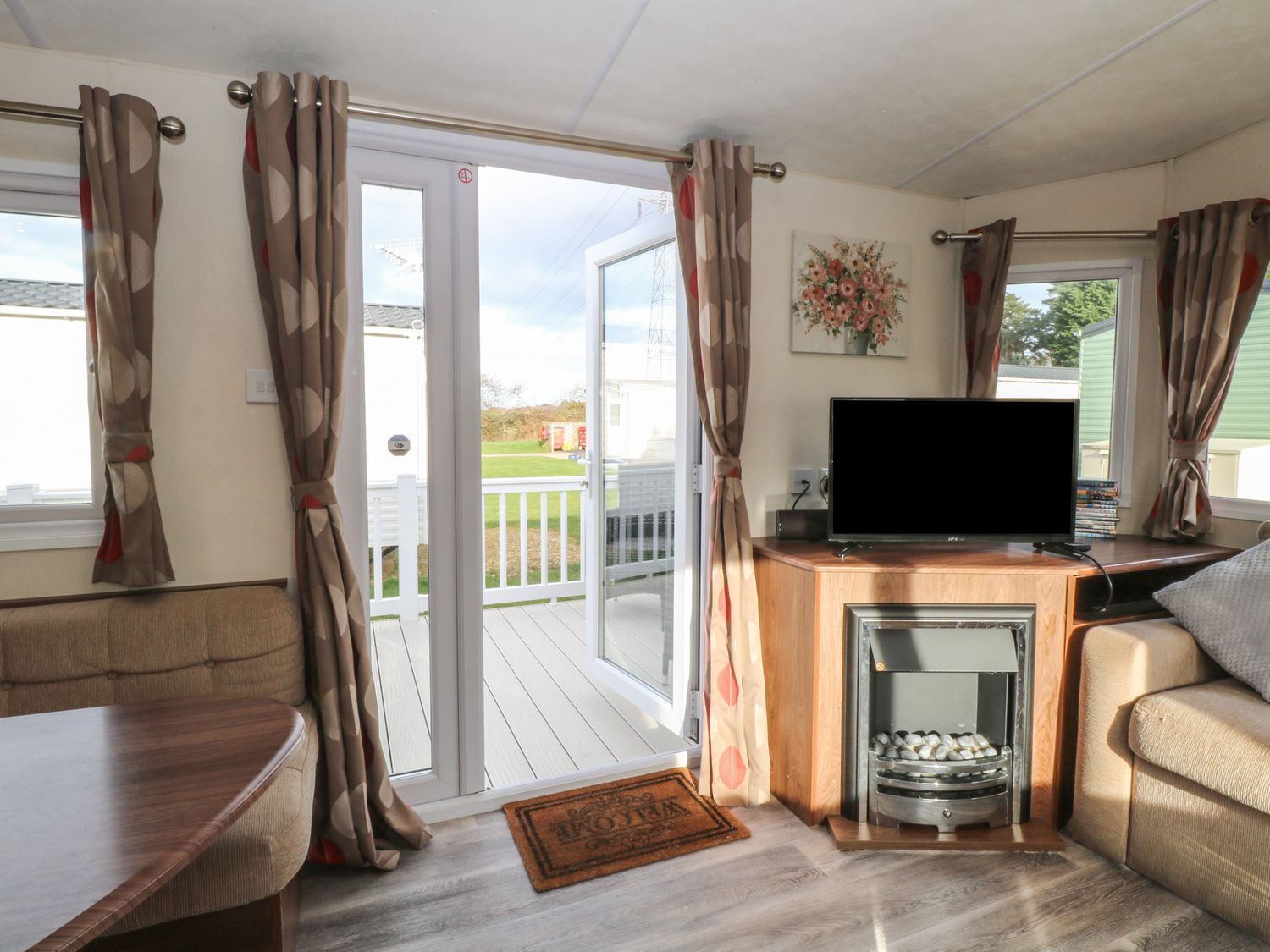 Ein gemütliches Wohnzimmer mit einer Couch, einem Fernseher, einem Kamin und einer Glastür, die auf eine Terrasse führt.