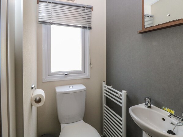 A small bathroom with a toilet, a window with blinds, a radiator, and a sink. - 46 Foxburrow Hang (Great Yarmouth)