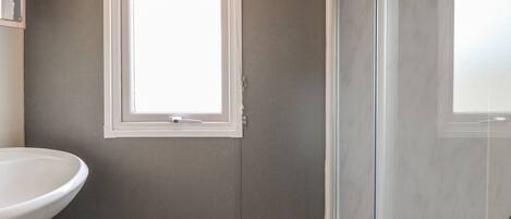 A bathroom with a white sink, a window with blinds, and a glass shower enclosure.