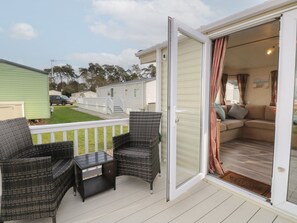 A covered outdoor area with wicker furniture, a sliding glass door leading to a living room, and a view of neighboring mobile homes. - 46 Foxburrow Hang (Great Yarmouth)