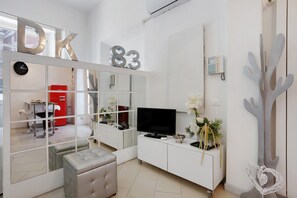 Un salon moderne avec un téléviseur, des meubles blancs, un meuble rouge et des éléments décoratifs, comme un cactus et un objet décoratif en forme de cœur.