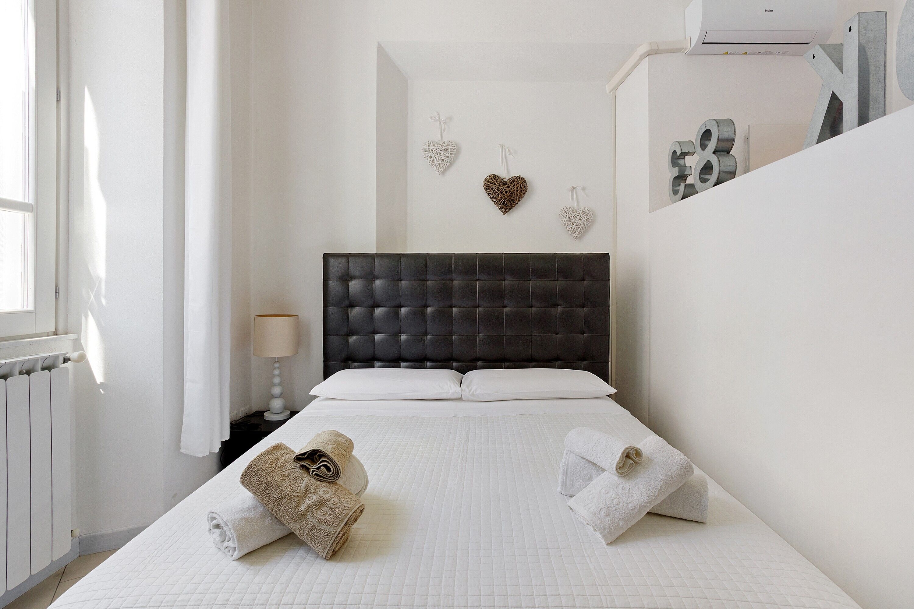A bedroom with a dark headboard, white bedding, heart-shaped wall decorations, and a radiator.